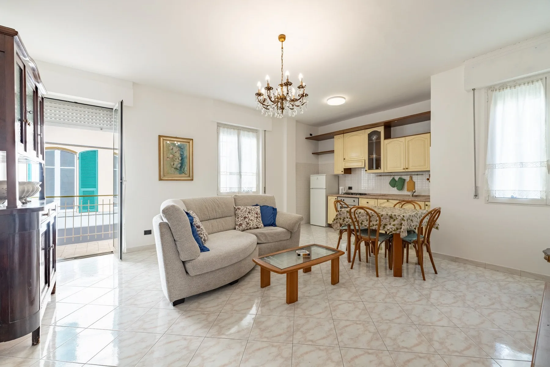 A bright living and dining area with a sofa, table, and adjoining kitchen.