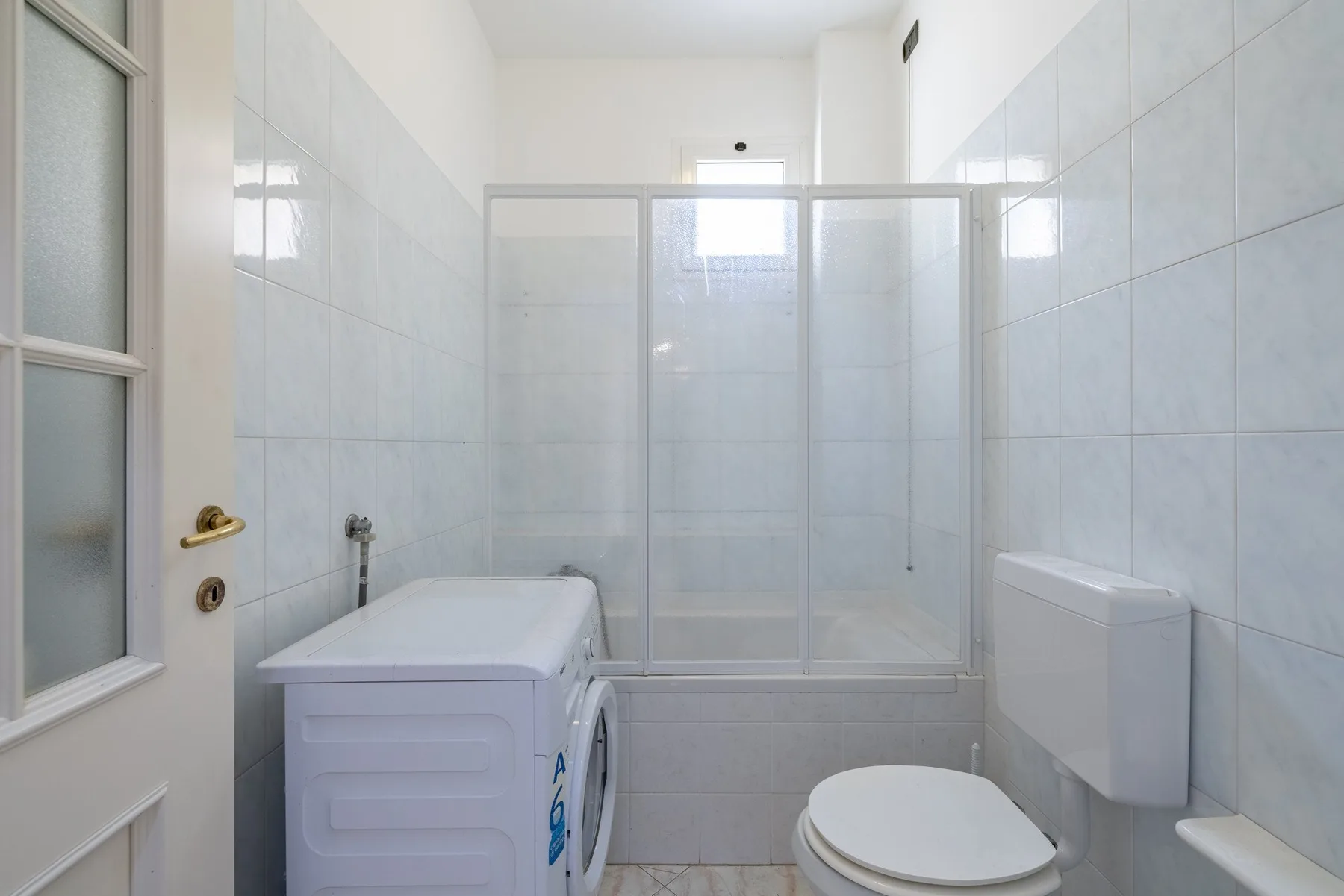 A tiled bathroom with a shower, toilet, and washing machine.