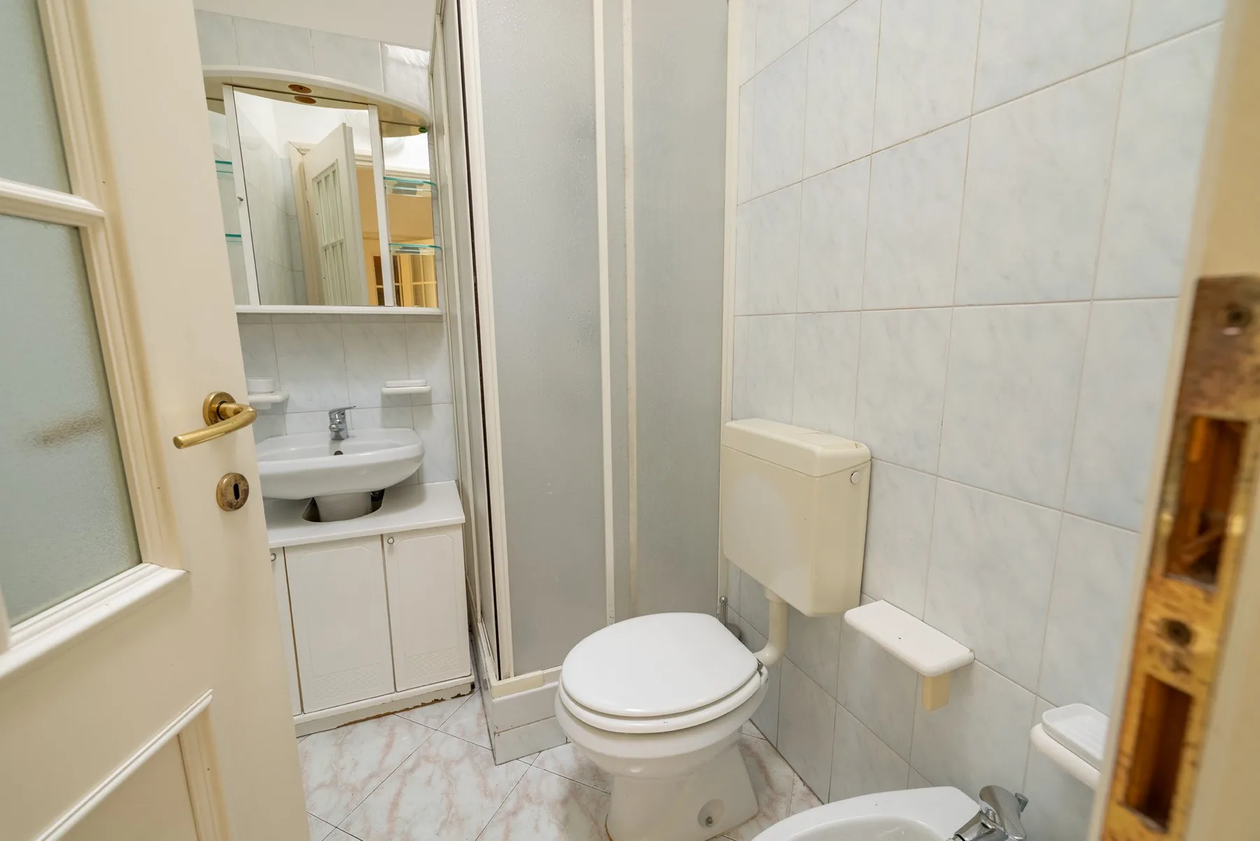 A tiled bathroom with a toilet, sink, and wall mirror.