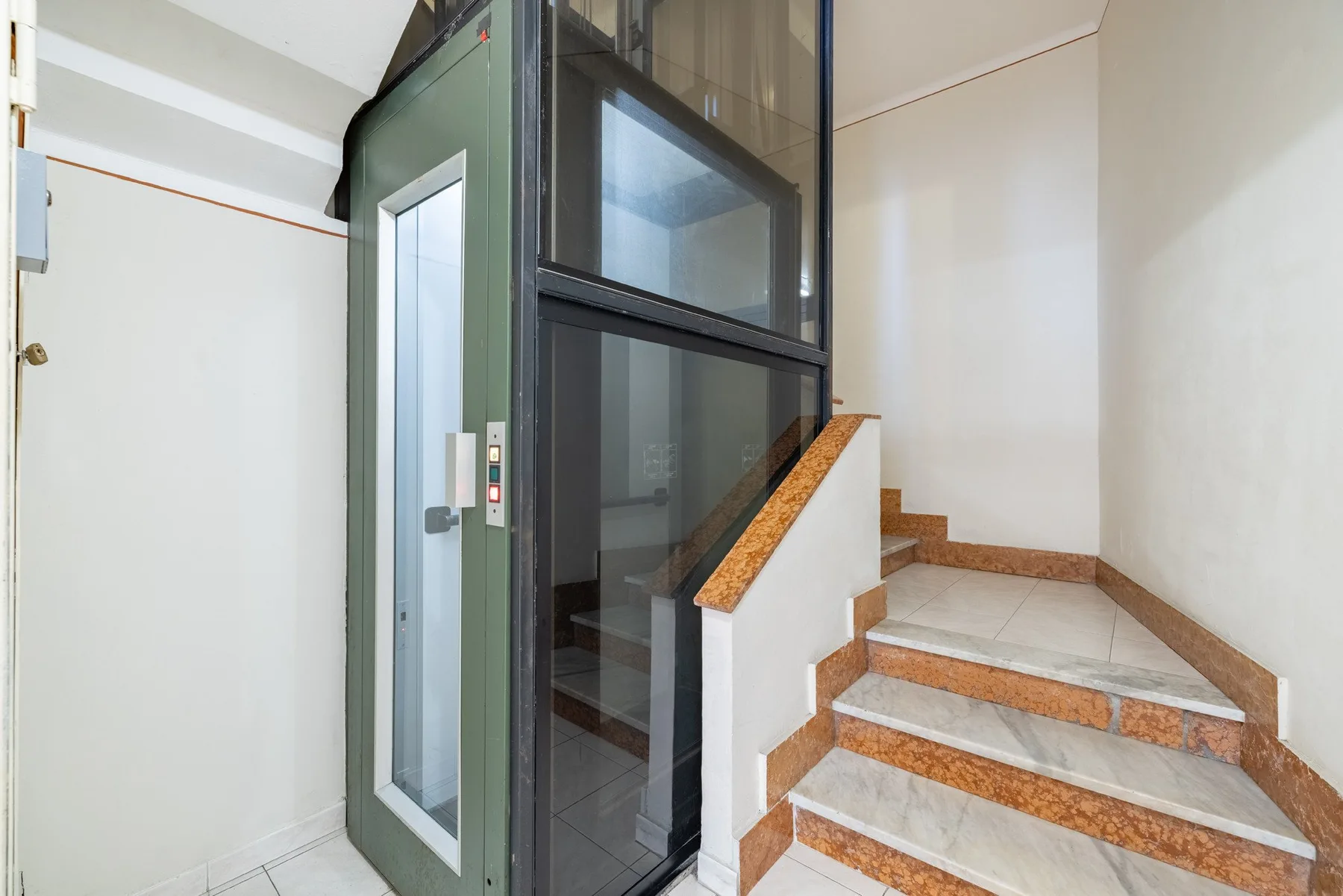 An indoor stairwell with a glass elevator beside the steps.