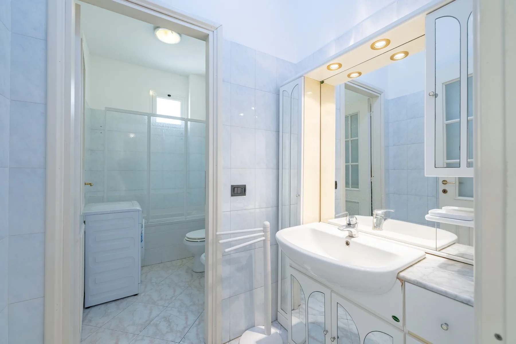 A bright tiled bathroom with a sink and a glass shower enclosure.