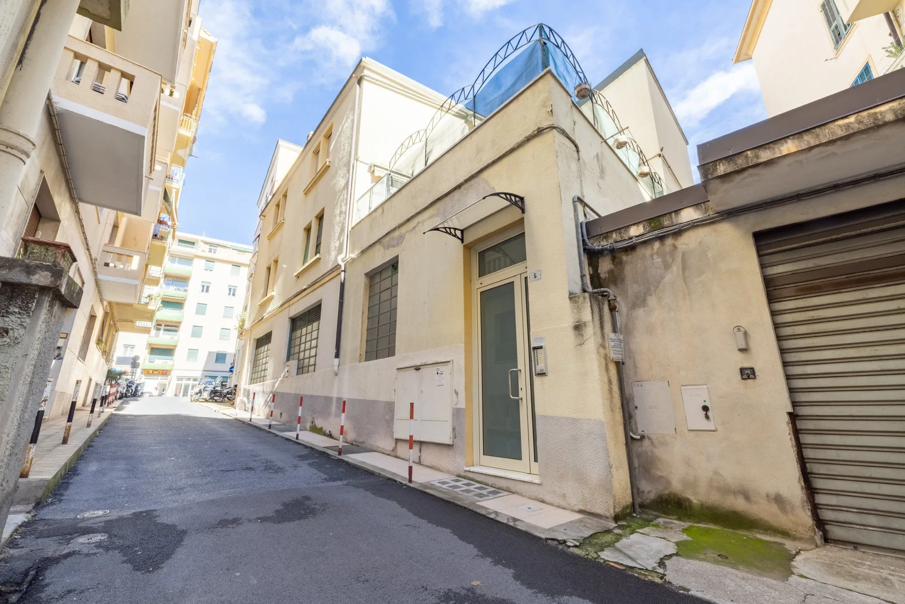 A narrow paved lane runs between closely spaced buildings under a blue sky.