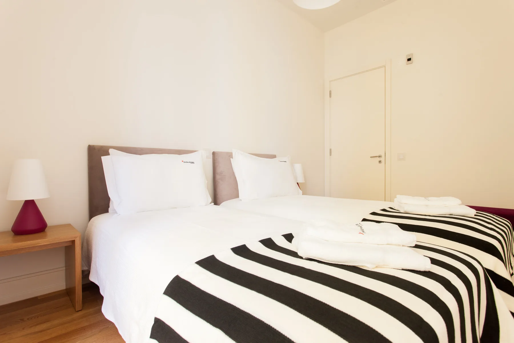 A bedroom with white bedding and black striped blankets.