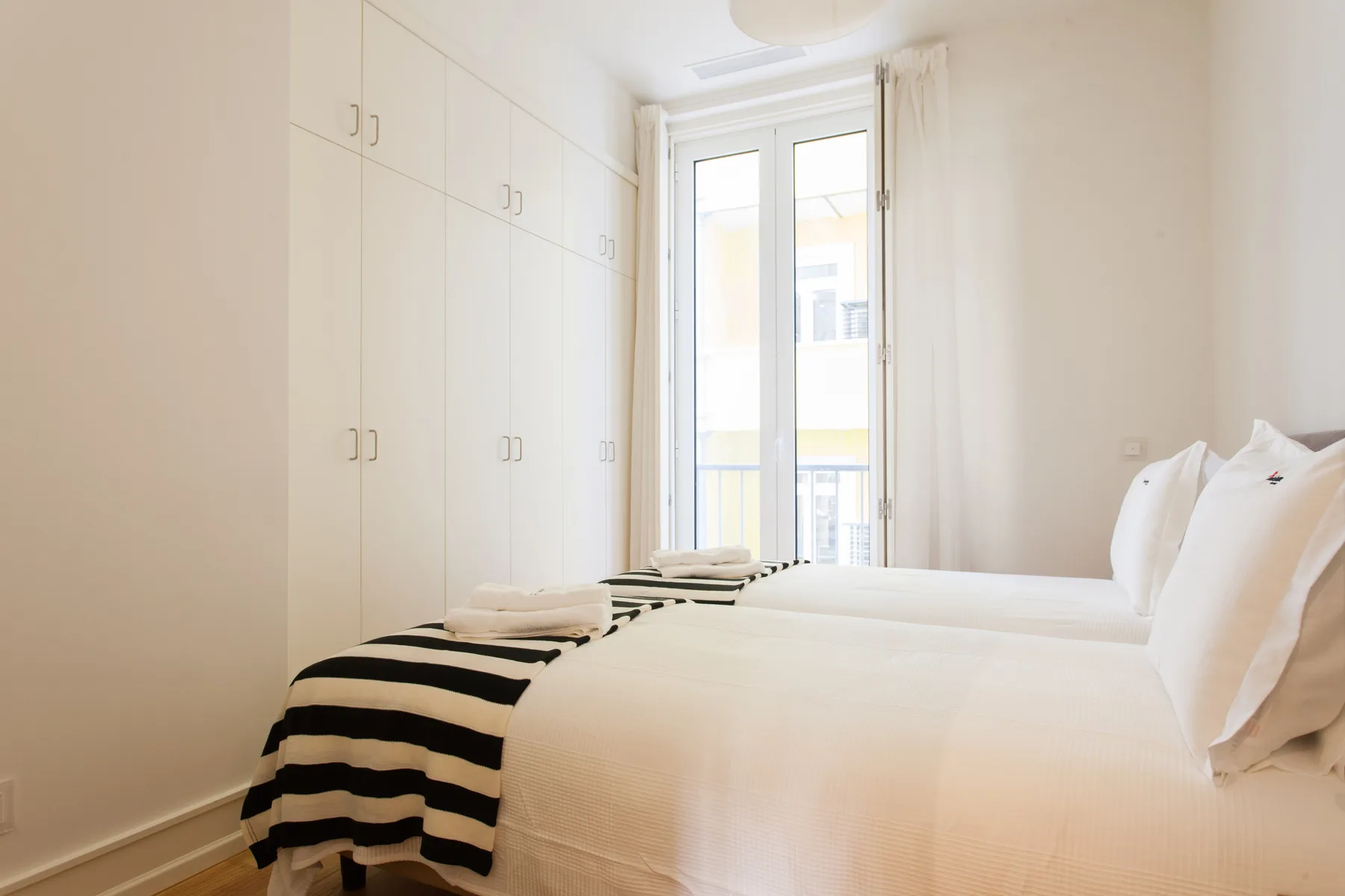 A bright bedroom with beds, white bedding, and built-in wardrobes.