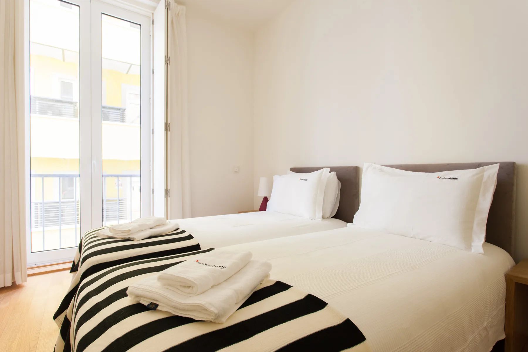 A bright bedroom with white bedding and a tall window.