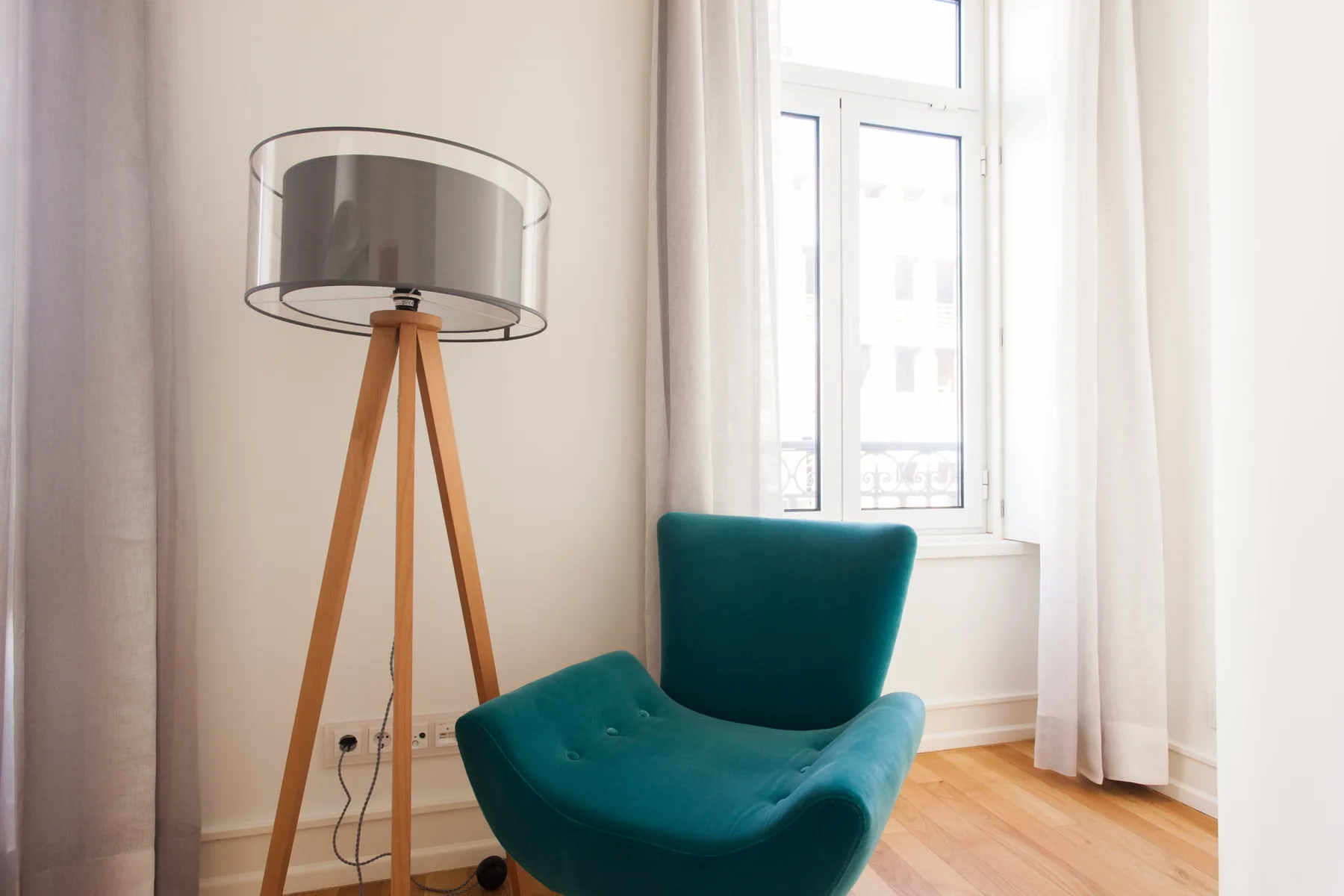 A bright living area with a teal chair beside a tall floor lamp and window.
