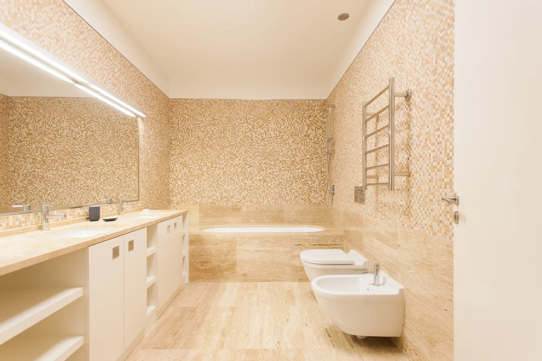 A bright bathroom with a long vanity, bathtub, toilet, and bidet.