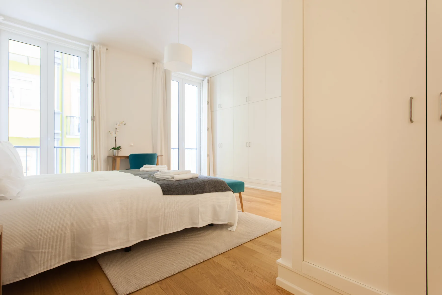 A bright bedroom with a neatly made bed and a large built-in wardrobe.