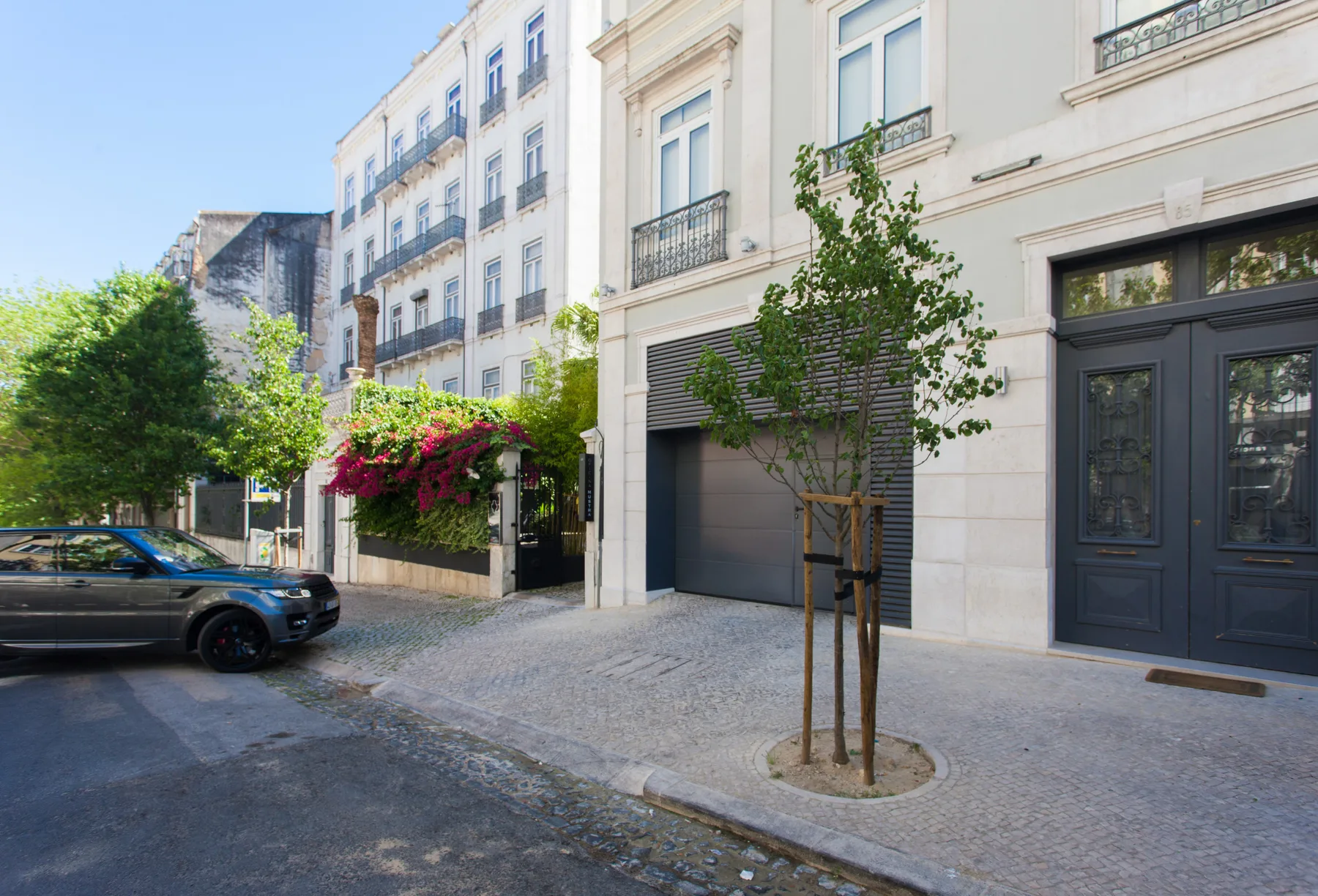A city street with pale building facades, a parked vehicle, and sidewalk trees.