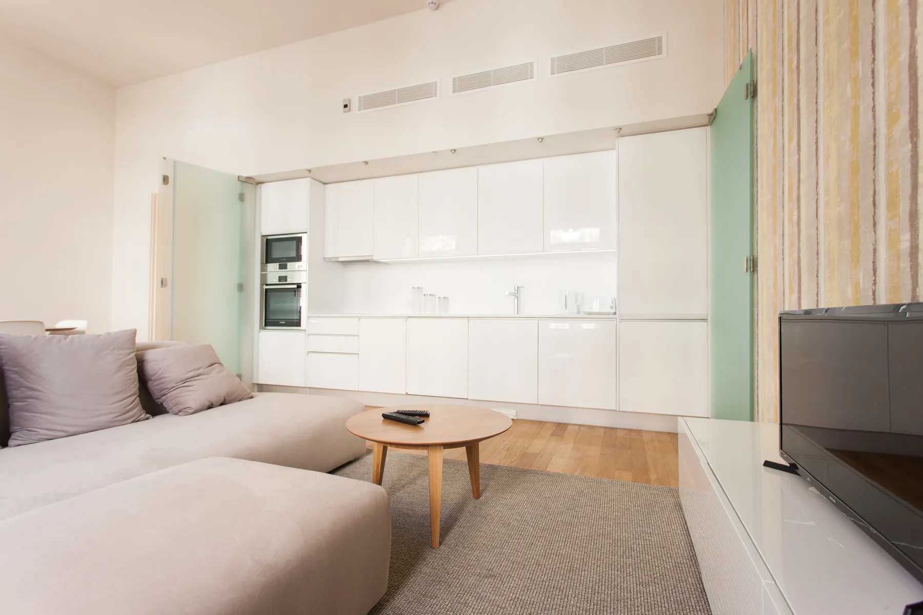 A bright living area with a sofa, coffee table, and white kitchen cabinets.