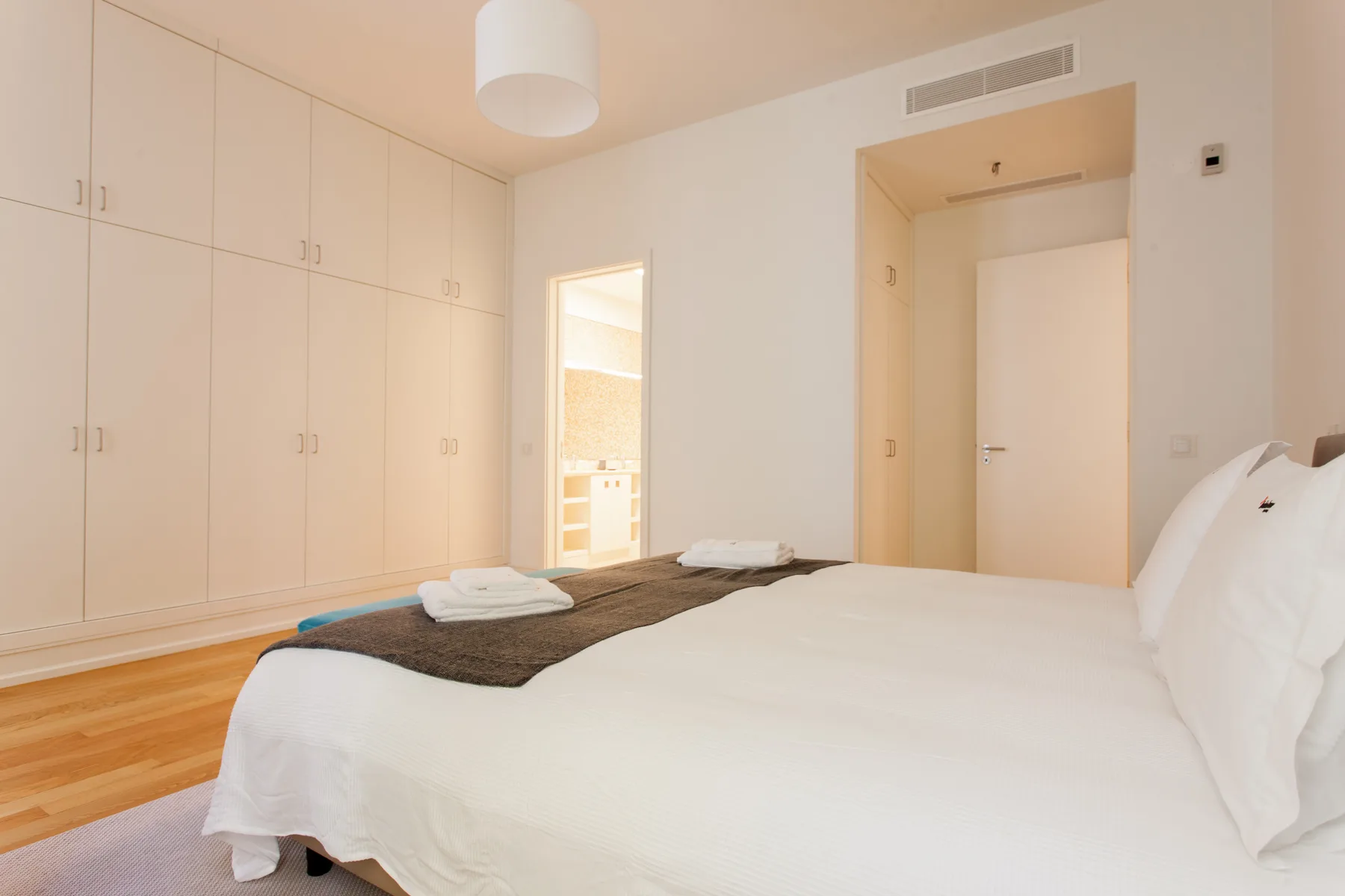 A bright bedroom with a white bed and built-in cabinets along the wall.
