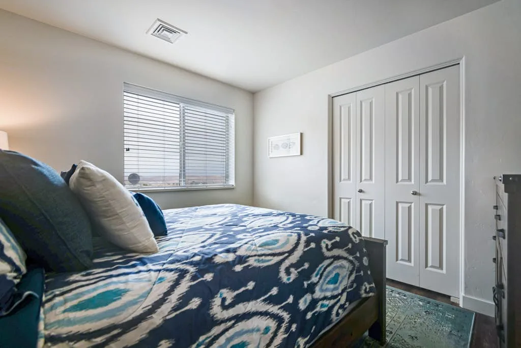 Un dormitorio con una cama cubierta por una colcha azul estampada junto a una ventana.