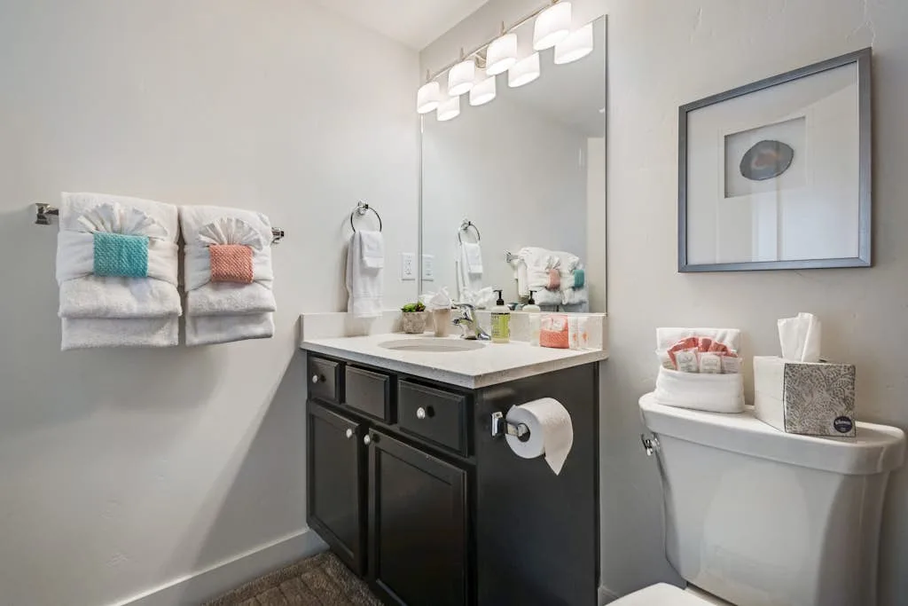 Un tocador de baño con lavabo y espejo está junto a un inodoro.