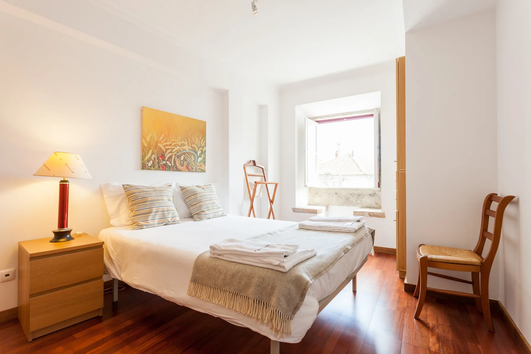 Un dormitorio luminoso con una cama bien hecha y una ventana.