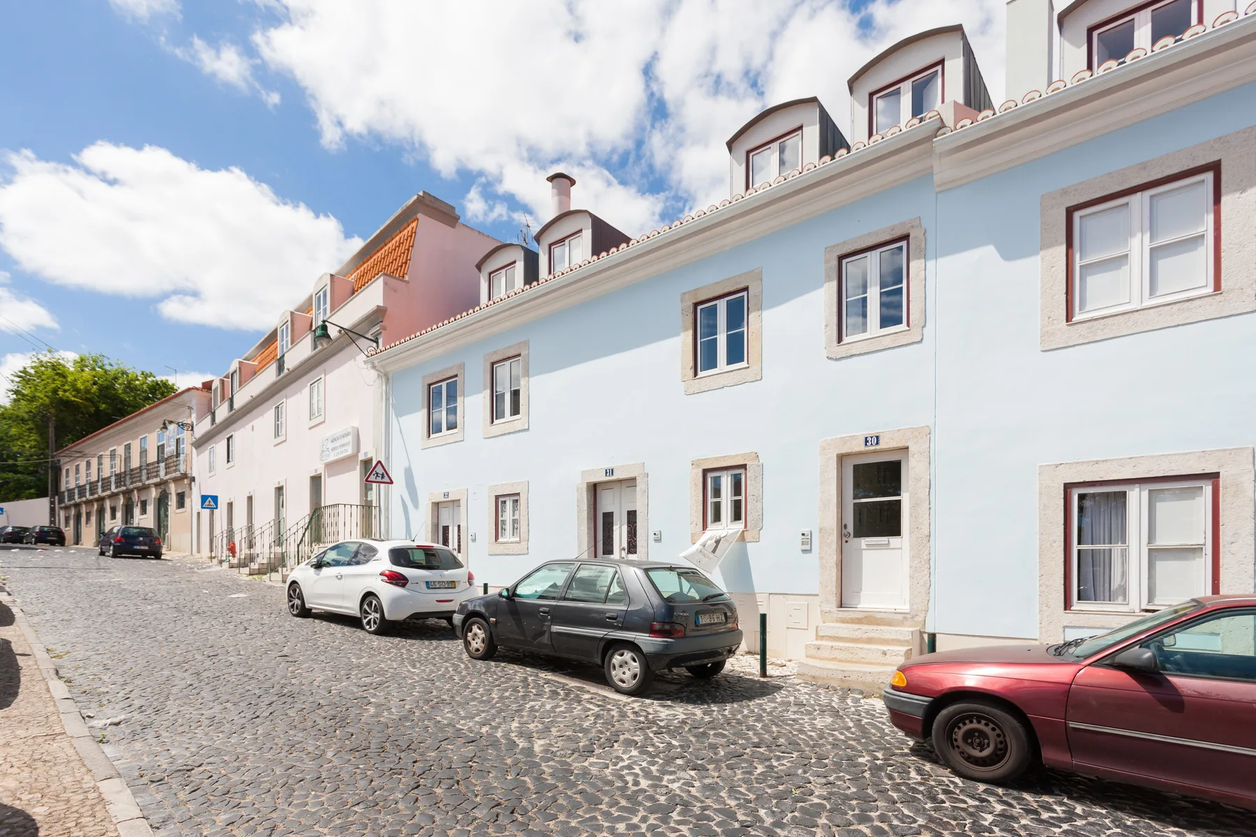 Una hilera de edificios de colores pastel bordea una calle adoquinada con coches estacionados.