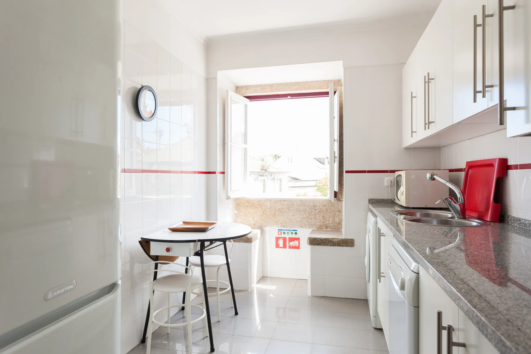 Una cocina luminosa con una pequeña mesa de comedor junto a una ventana abierta.