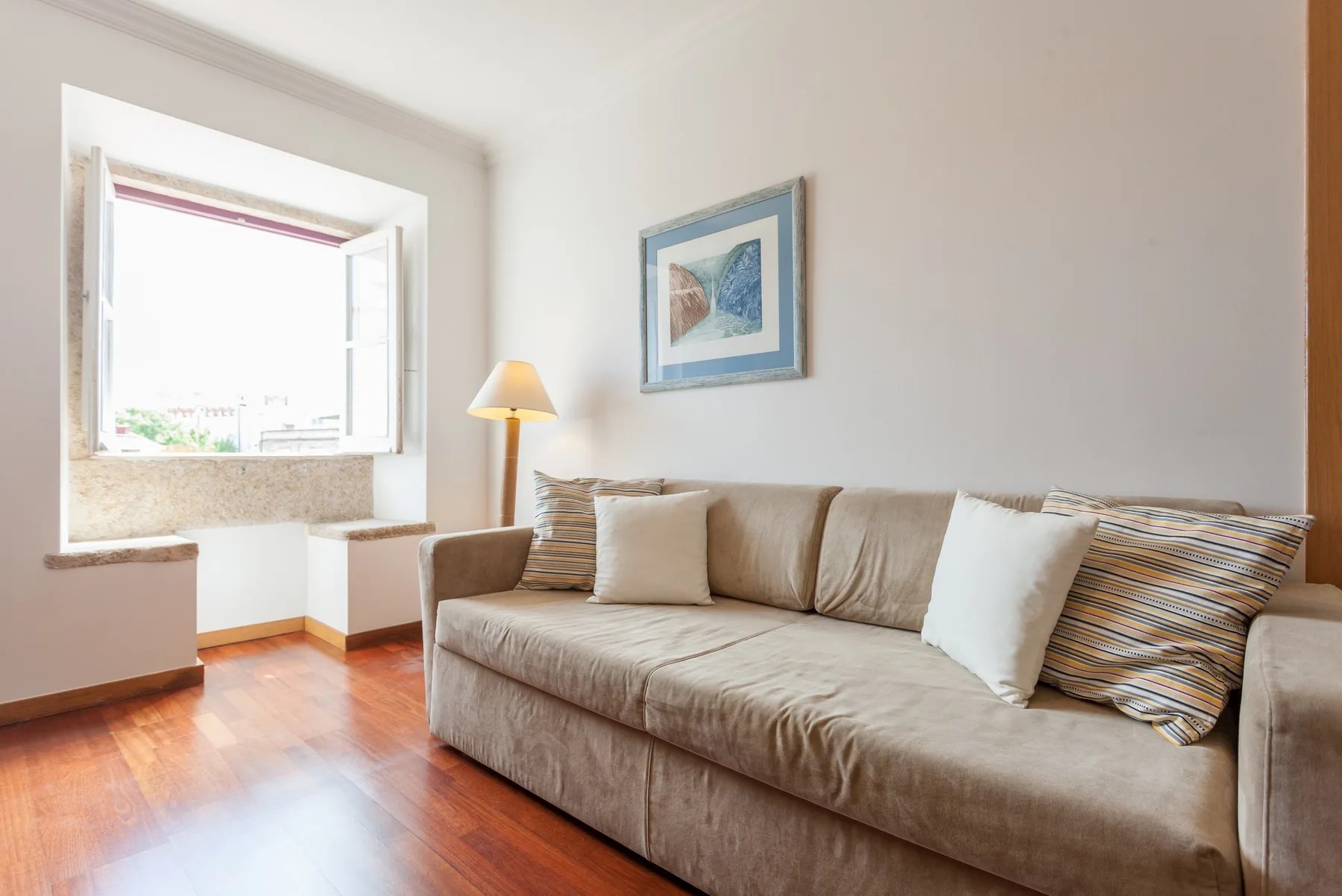 Una sala luminosa con un sofá beige junto a una ventana amplia.