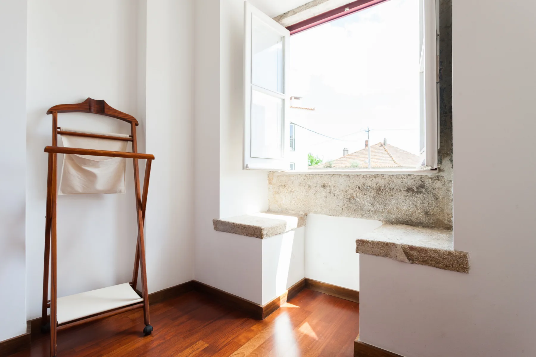 Una habitación luminosa con una ventana abierta y un perchero de madera.