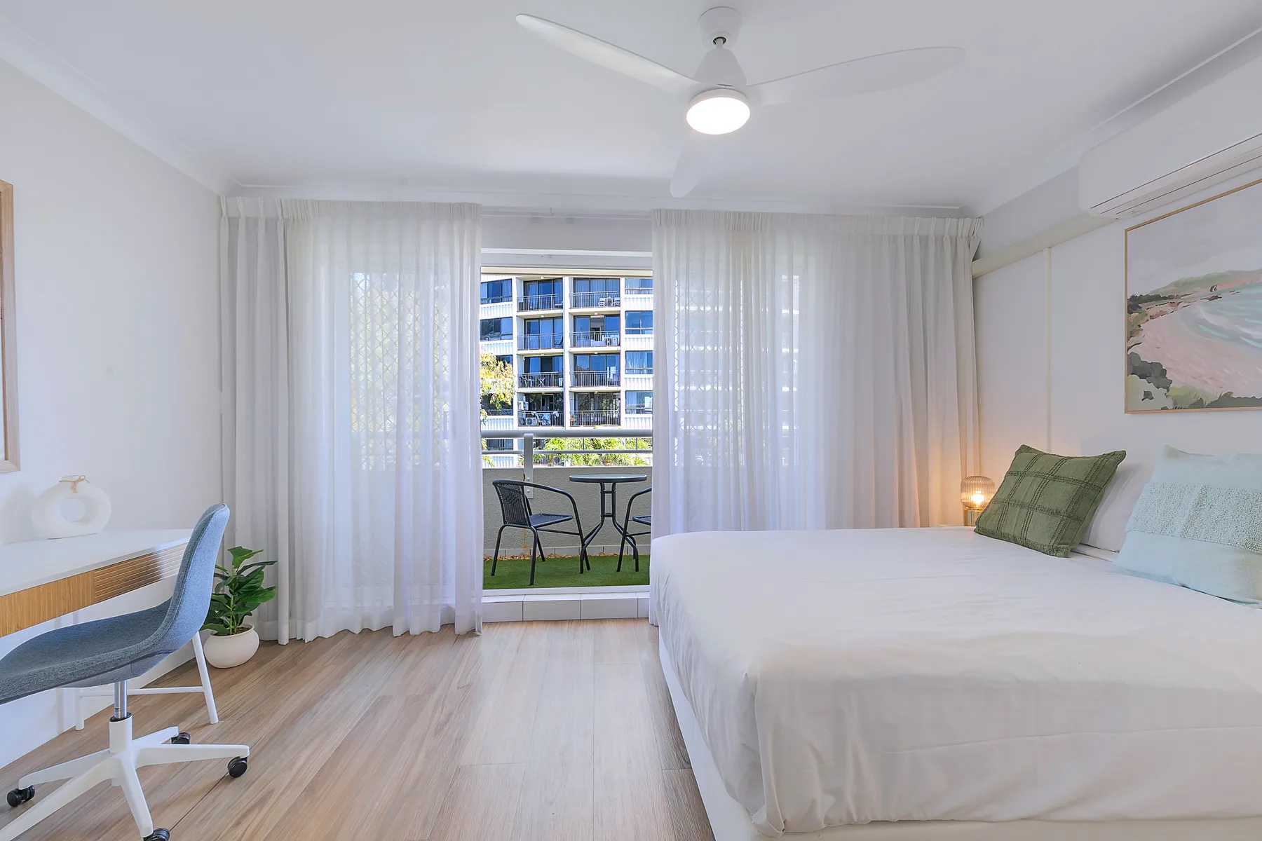 Un dormitorio luminoso con una cama, un escritorio y puertas corredizas que dan a un balcón.