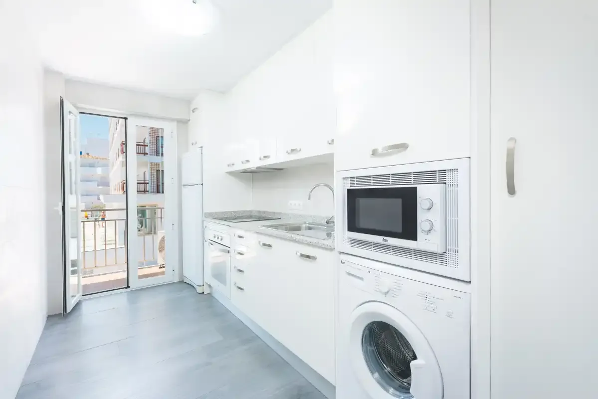 Bright white kitchen with built-in appliances and glass doors opening onto a balcony.