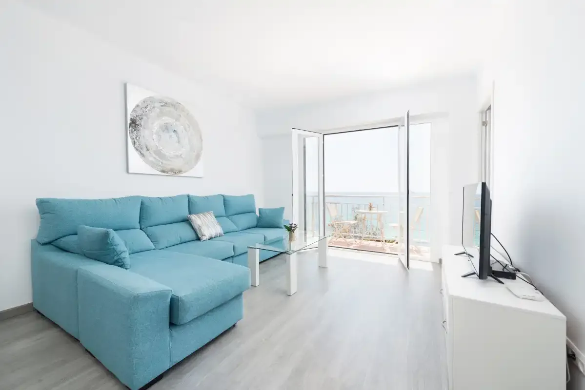 A bright living room with teal seating and open glass doors to a balcony.