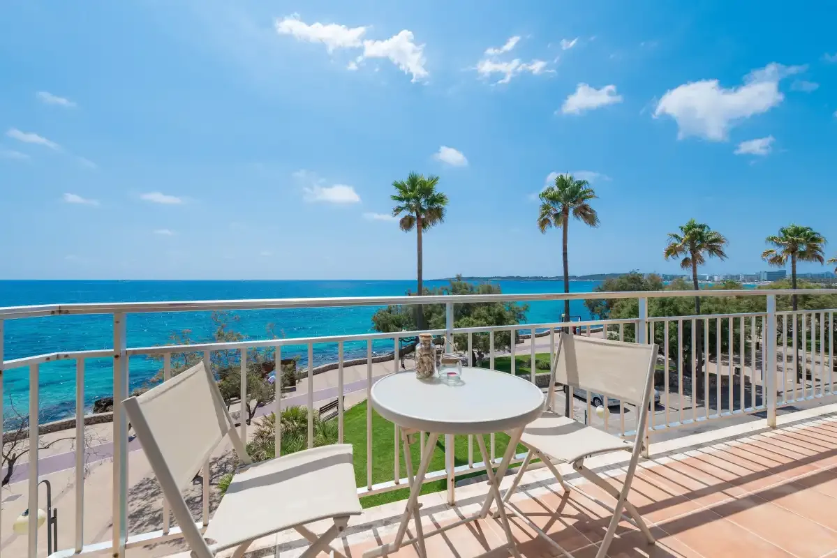 A seaside terrace with outdoor seating overlooks the blue water and palm trees.
