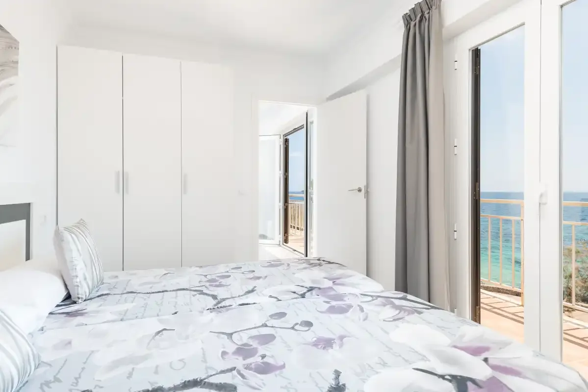 A bright bedroom with a patterned bed and glass doors opening onto a balcony.