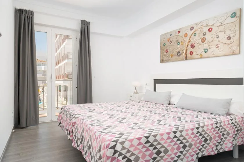 A bedroom with a large bed, gray curtains, and colorful wall art.