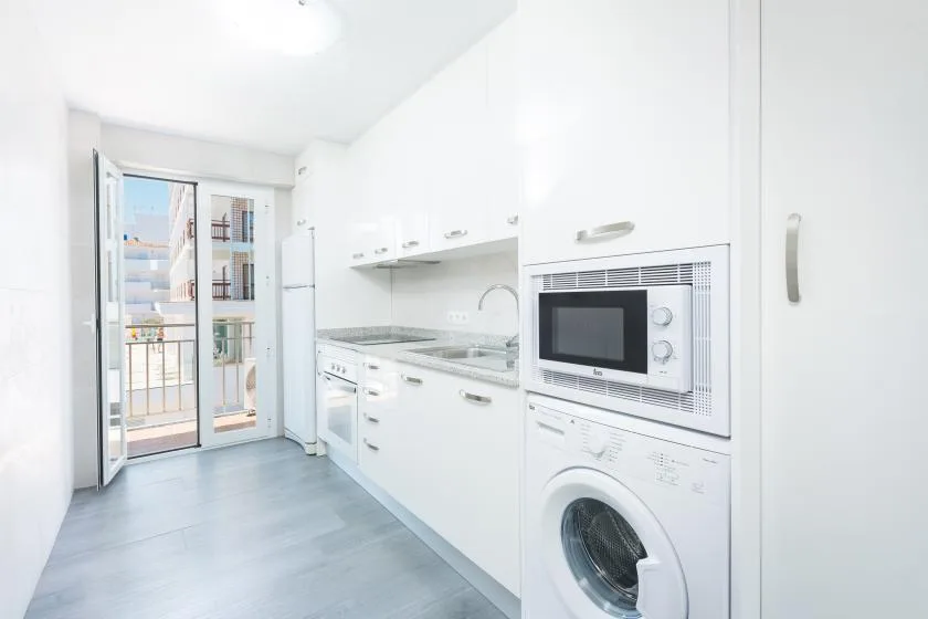 A bright white kitchen with built-in appliances and glass doors opening to a balcony.