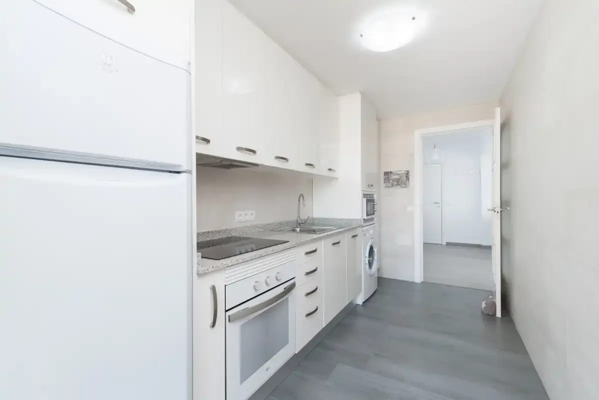A bright white kitchen with cabinets, an oven, and a washing machine.