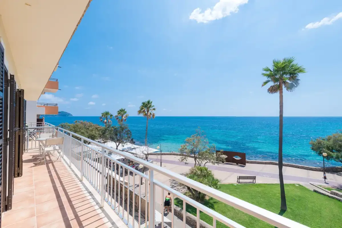 A seaside balcony overlooks the blue water, promenade, and palm trees.