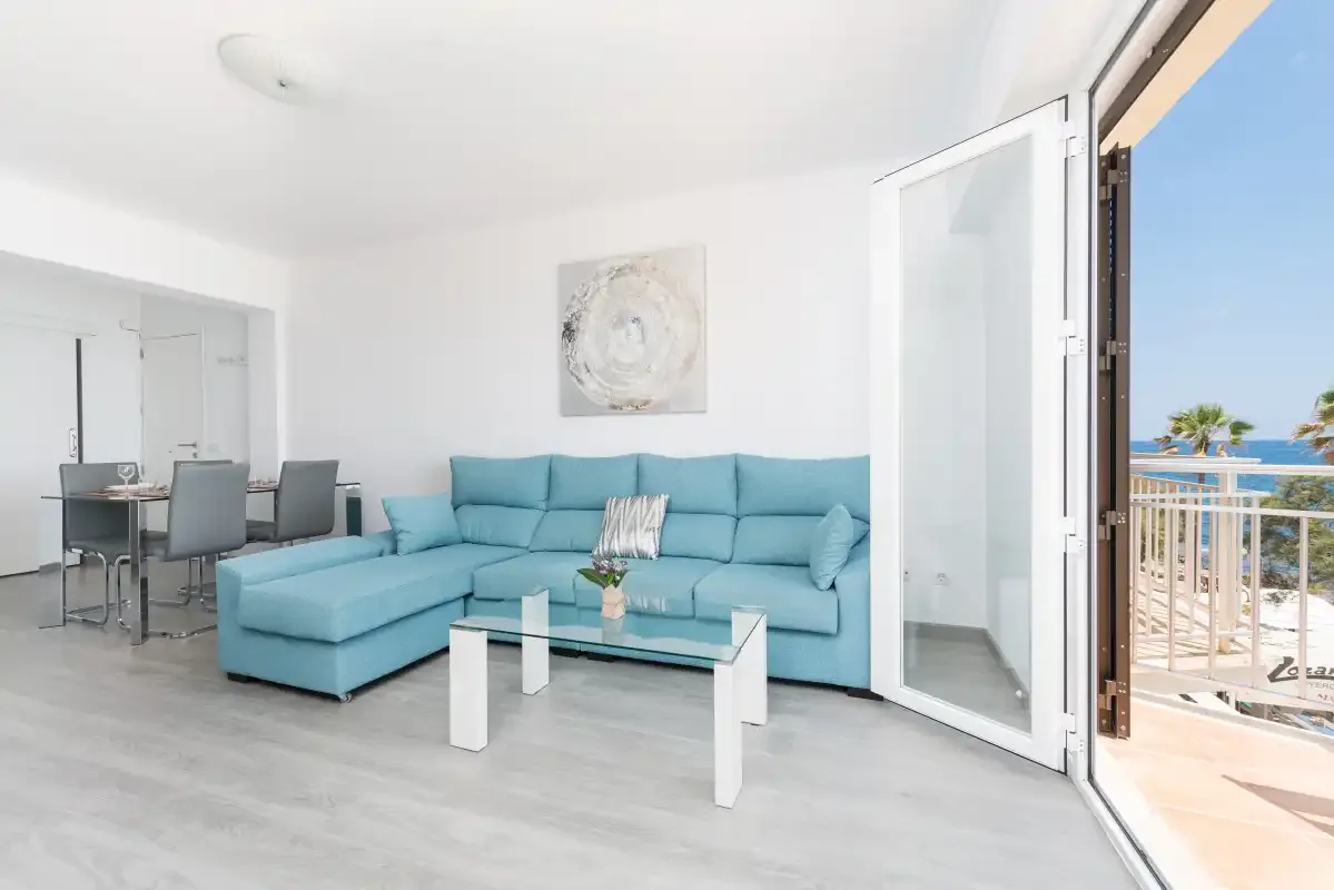 A bright living room with turquoise seating beside open balcony doors.