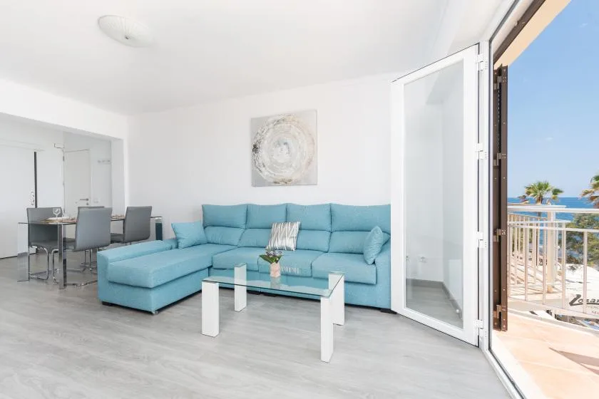 A bright living room with a turquoise sectional and an open balcony door.
