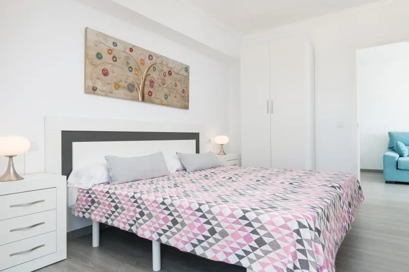 A bright bedroom with a patterned bedspread, bedside tables, and wall art.