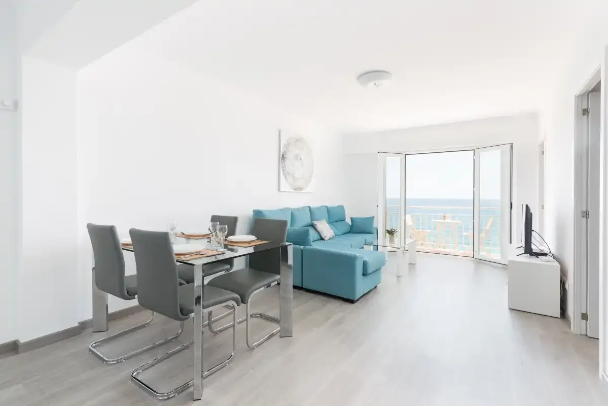 A bright living and dining area with a blue sofa and balcony doors.