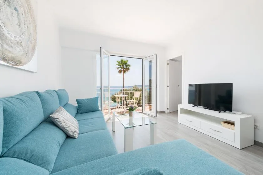 A bright living room with blue seating, a television, and open balcony doors.