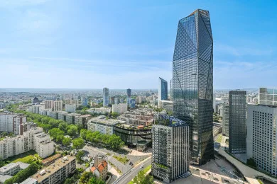 A city skyline with a prominent glass tower rising above surrounding buildings.
