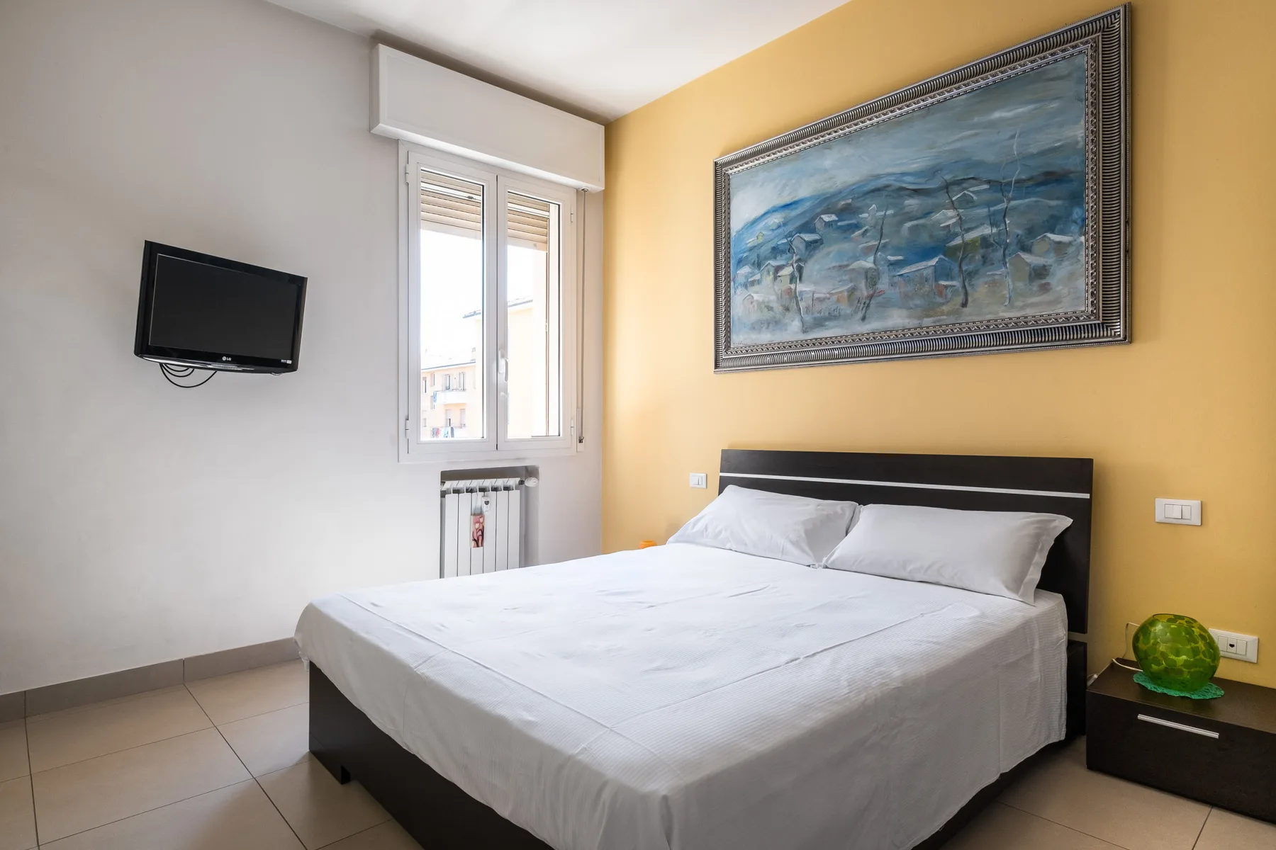 A bedroom with a double bed, a wall-mounted television, and framed artwork.