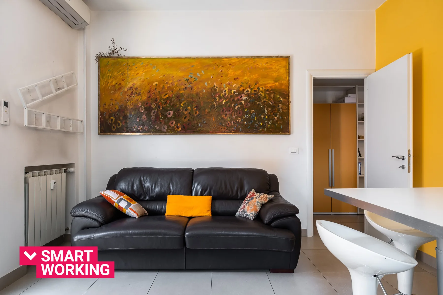 A living room with dark seating beneath a large abstract painting.