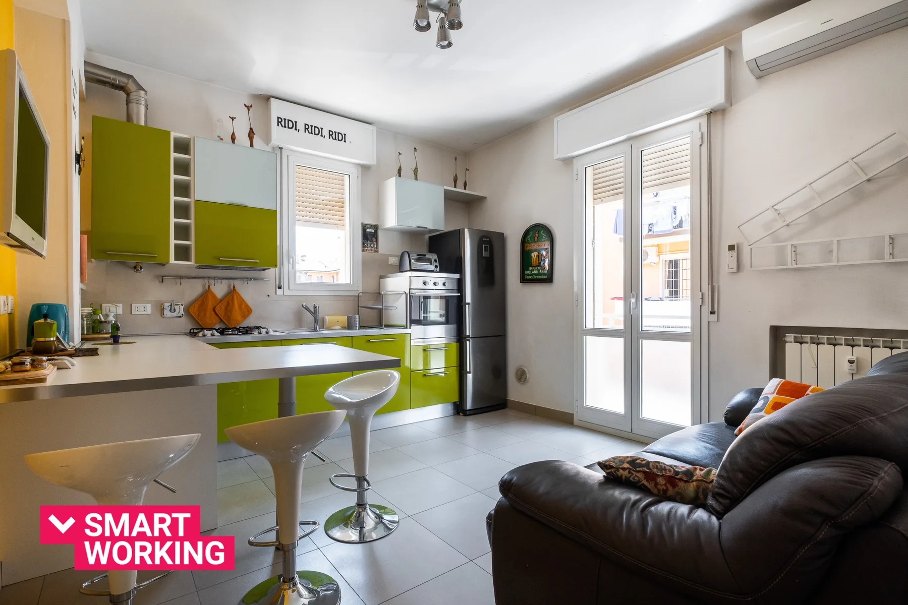 A bright open-plan kitchen and living area with green cabinetry and seating.