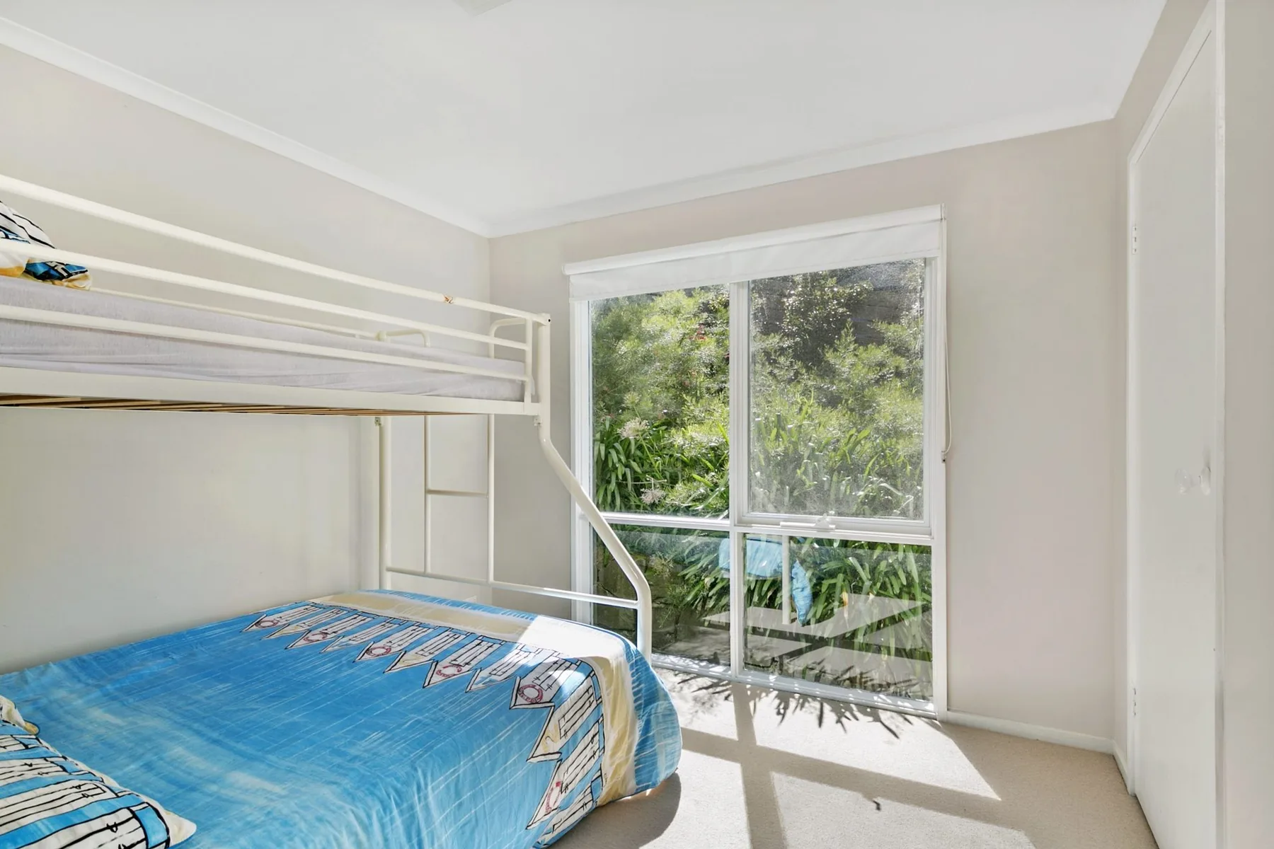A bedroom with a bunk bed beside a large window overlooking greenery.