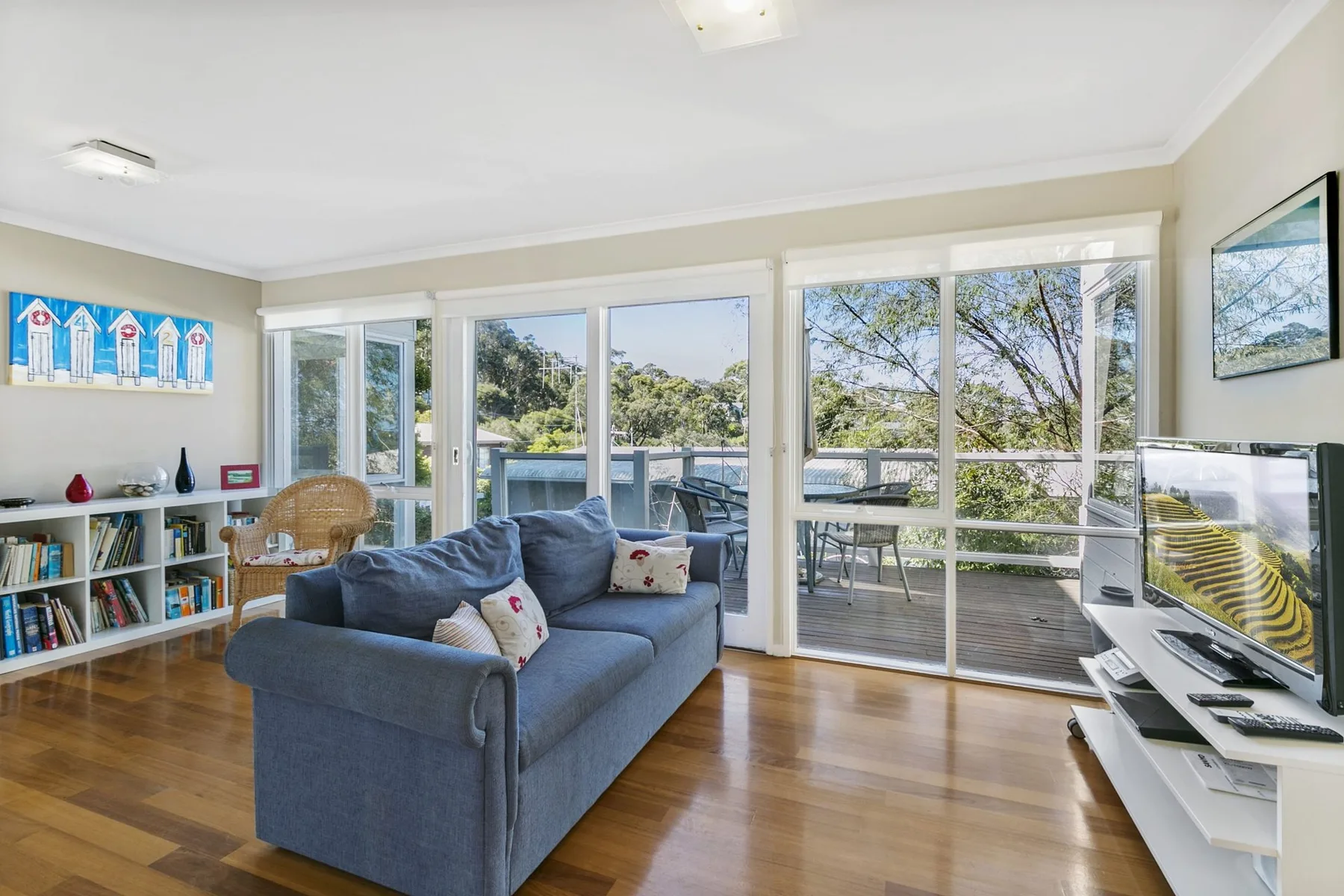 A bright living room with seating beside large windows overlooking trees.