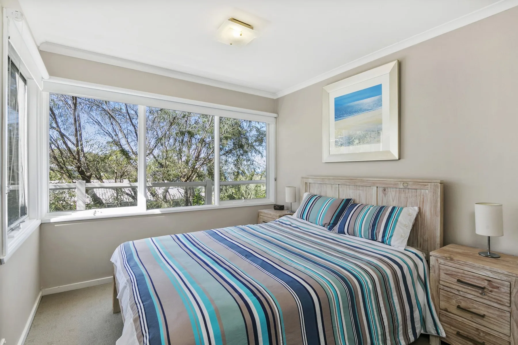 A bedroom with a striped bedspread and large windows overlooking trees.