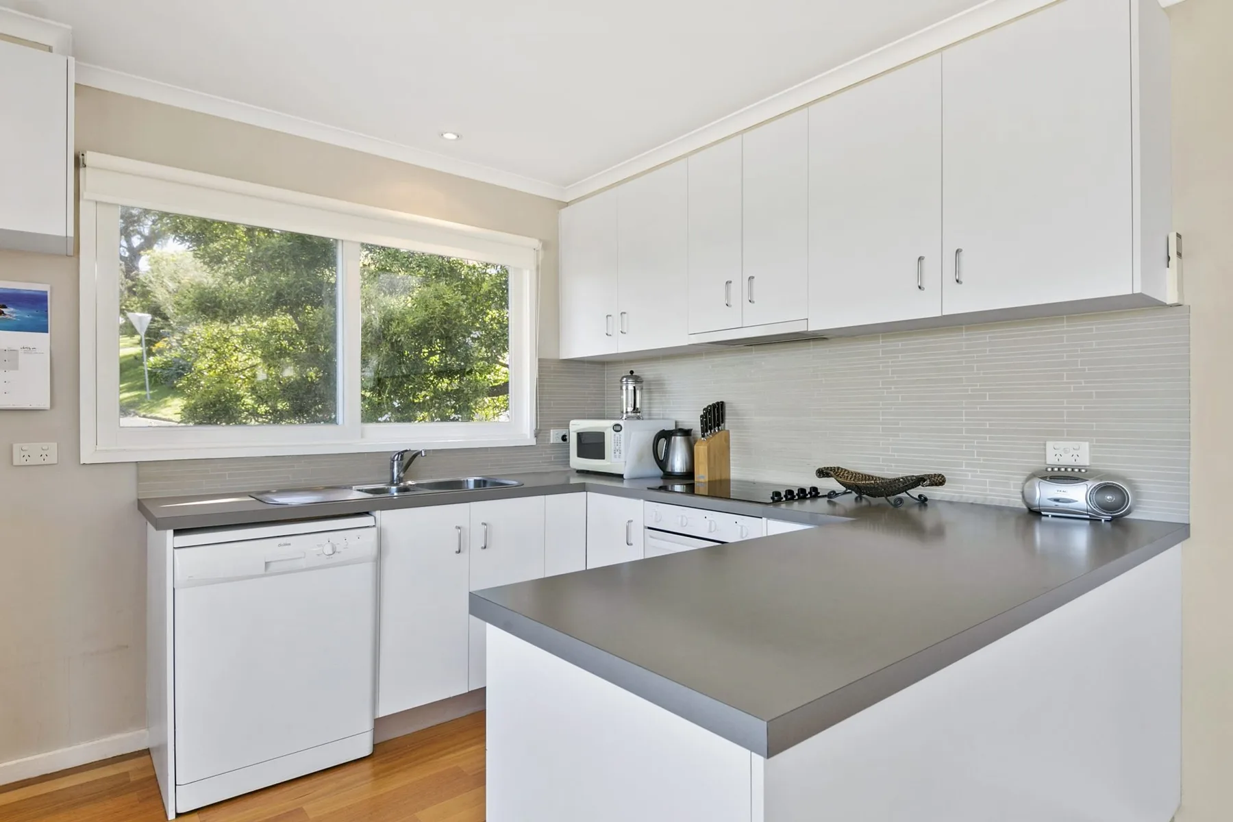 A bright kitchen with white cabinets and a wide window overlooking trees.