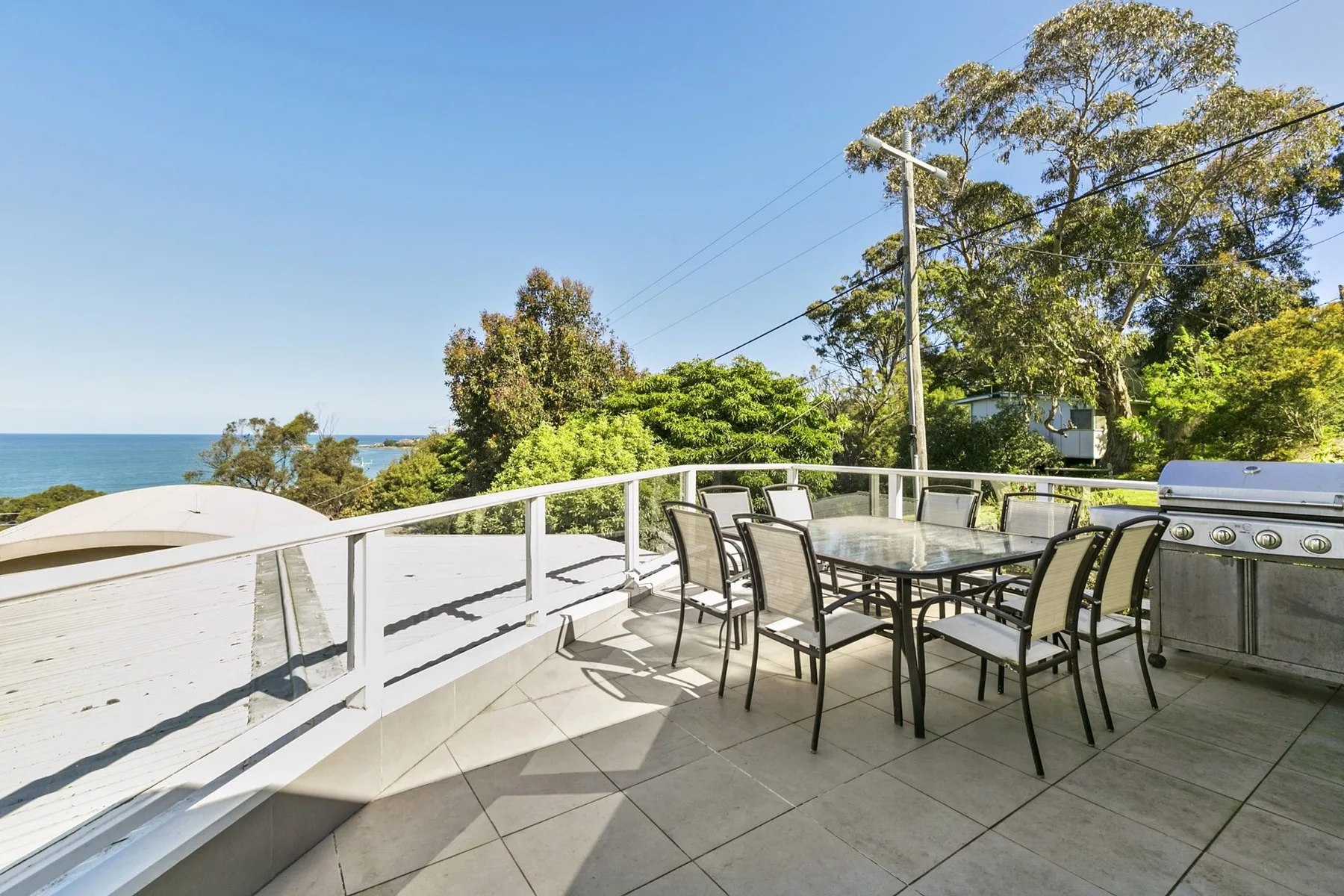 An outdoor dining area overlooks the water, with a table and seating on a tiled terrace.