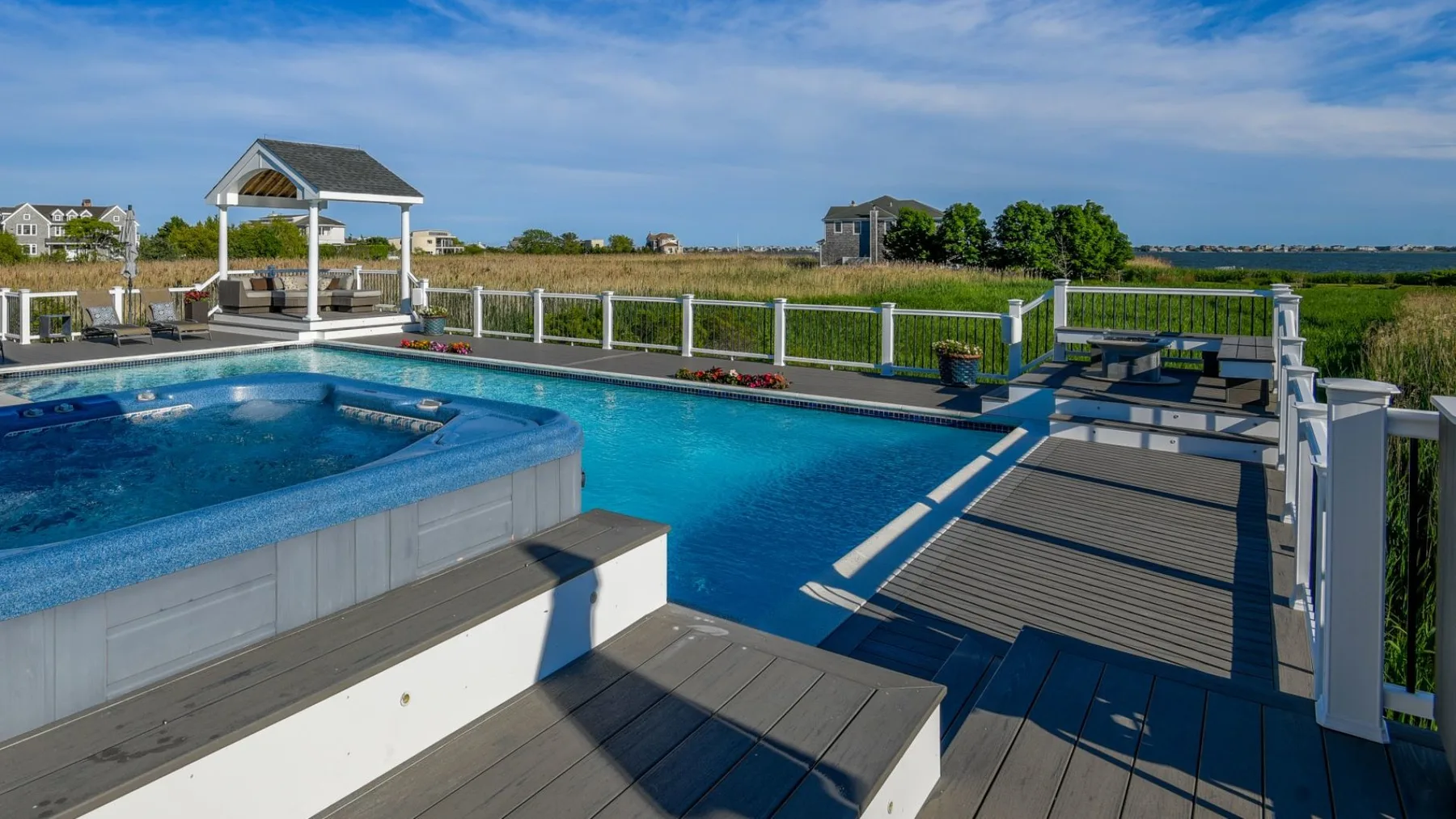 Una piscina al aire libre y un jacuzzi elevado están junto a una terraza de madera y una barandilla.