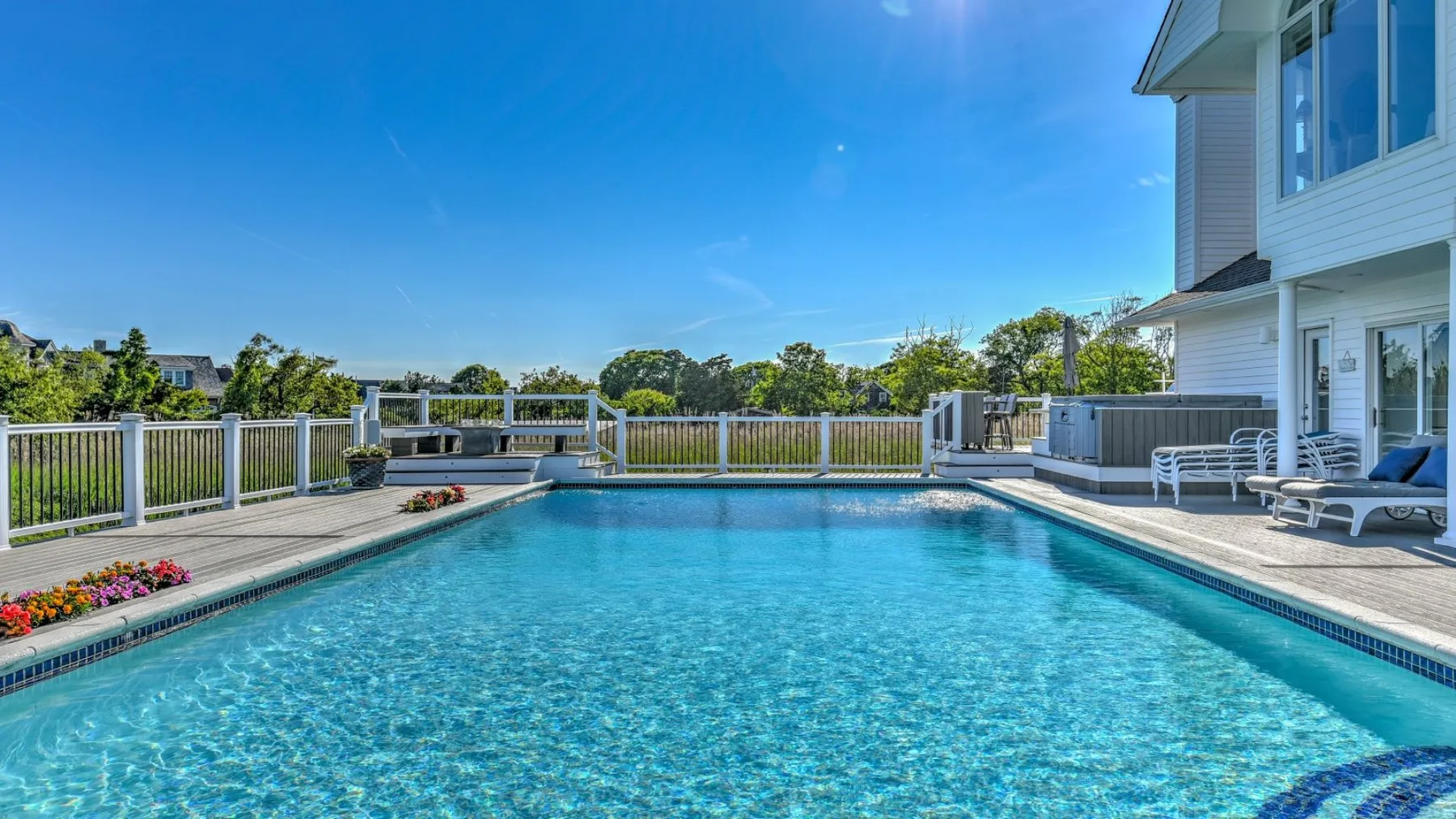 Una piscina al aire libre está junto a una casa blanca y un patio cercado.