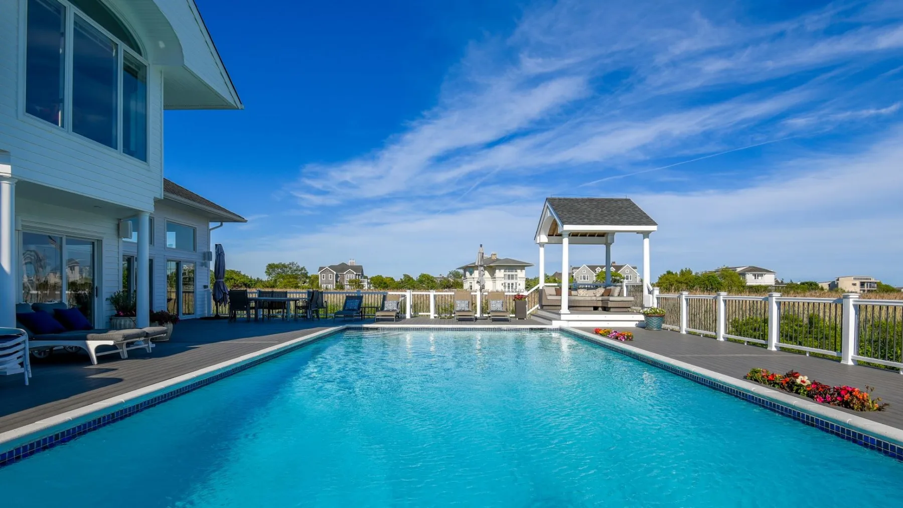 Una piscina al aire libre junto a una casa, con una zona de estar cubierta al fondo.