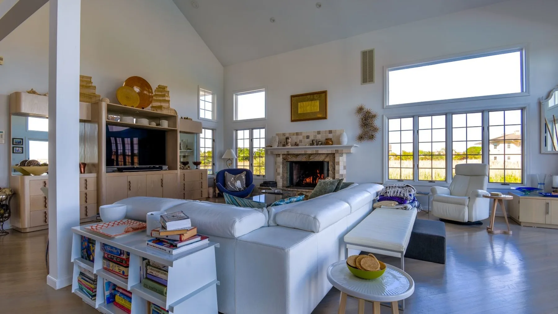 Una sala luminosa con asientos blancos alrededor de una chimenea y grandes ventanas.