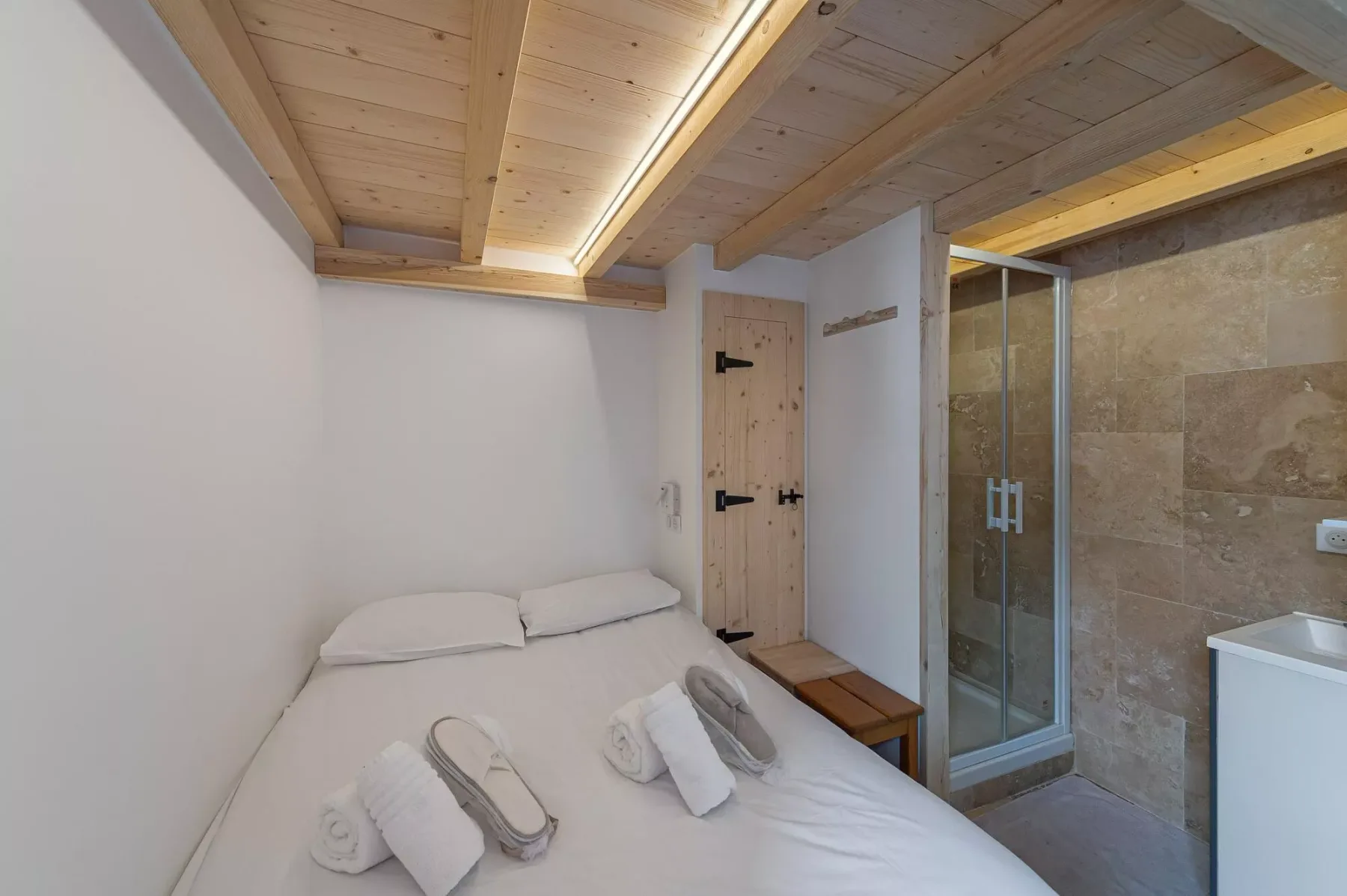 Un dormitorio con una cama blanca junto a una ducha de vidrio.